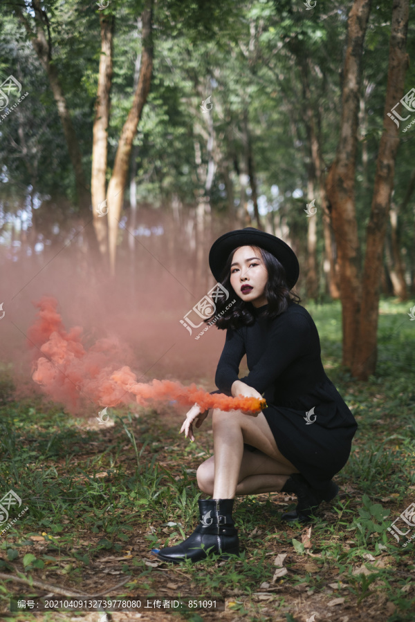 一个黑衣女巫在森林里玩橙色的烟火。