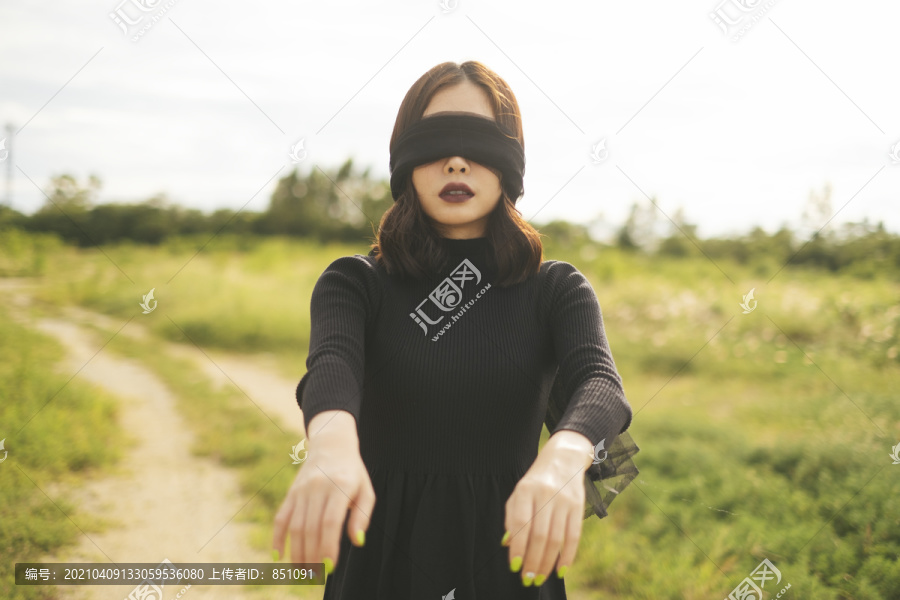 站在田野里的黑人新娘正试图戴着用面巾做的眼罩走路。