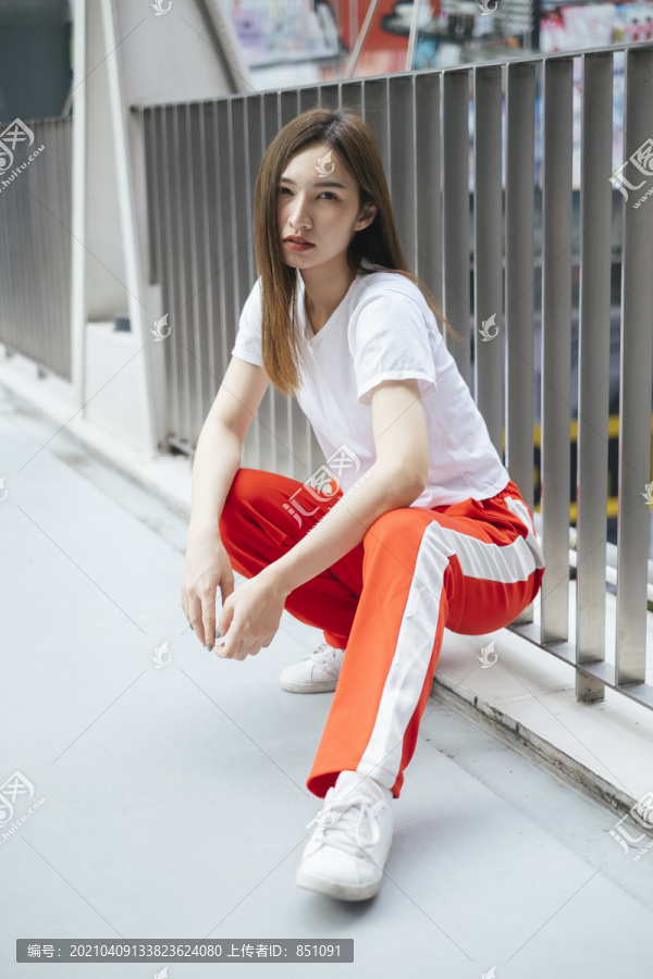 时尚写真-穿着白衬衫和红色运动裤的美丽亚洲年轻女子坐在地板上。