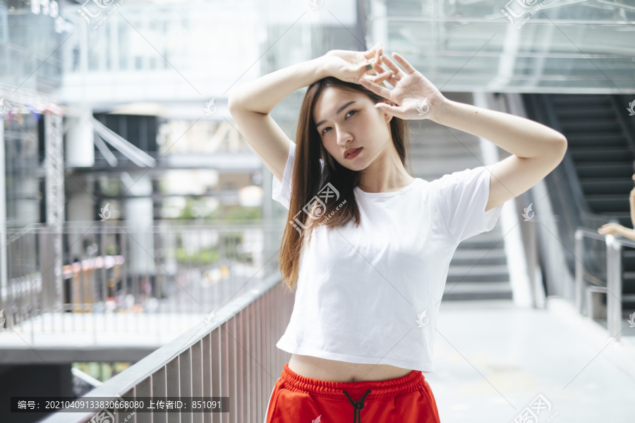 时尚写真-美丽的亚洲年轻女子穿着白衬衫和红色运动裤，性感的姿势双手放在头上。