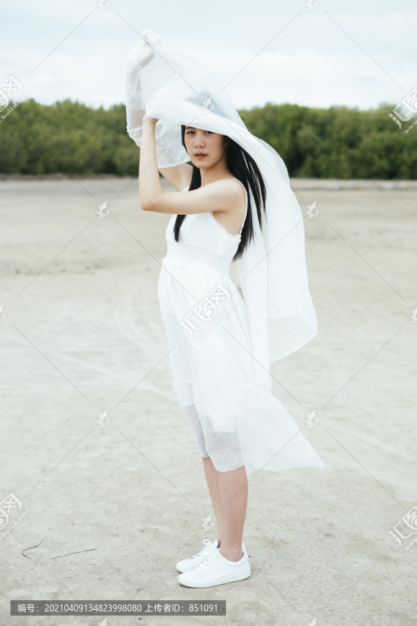 年轻的亚洲长黑发女子新娘的侧视图与白色面纱户外。