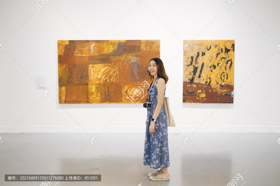 侧视图-美丽的时髦亚洲女子穿着蓝色连衣裙站在两个艺术画廊的杰作。