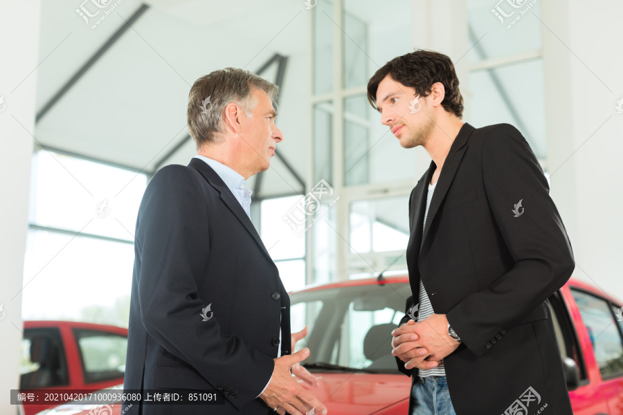 成熟的单身男子与红色汽车在轻型汽车经销商与一名男性客户，一个年轻人，他显然是买车或是一个汽车经销商