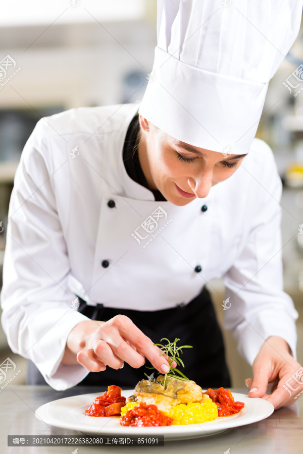 女厨师在酒店或餐厅的厨房里做饭，她正在完成盘子上的一道菜