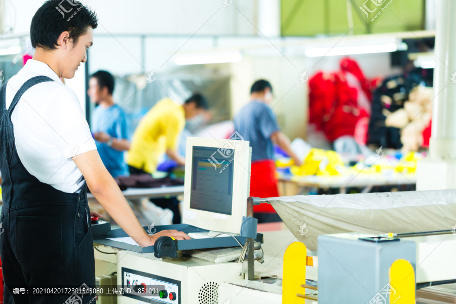 亚洲一家纺织厂的工人或生产经理在一台大机器的屏幕前工作
