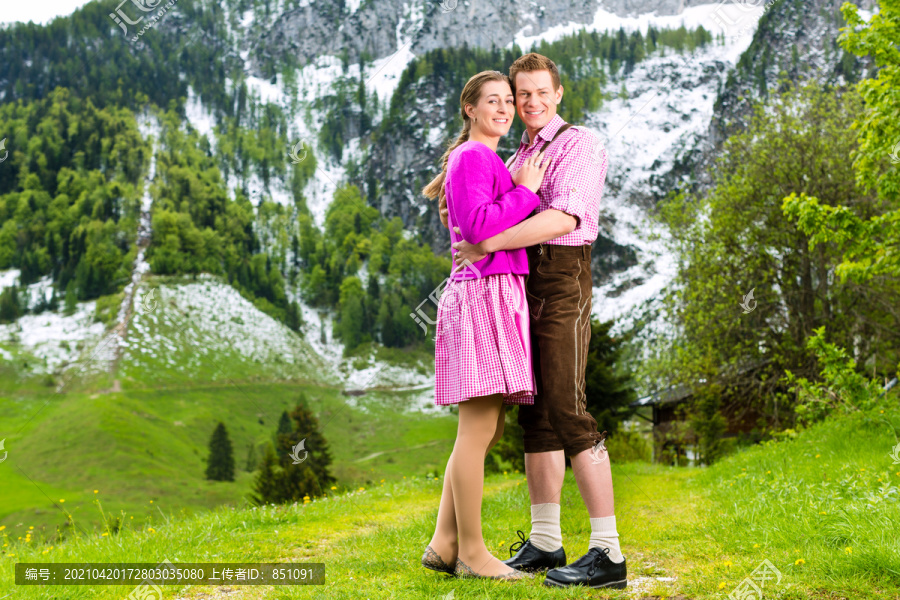 一对身着传统服饰的幸福夫妻站在草地上，山景尽收眼底