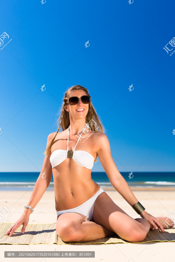 穿着白色比基尼的漂亮女人坐在沙滩上晒太阳，在蓝天下有很大的文案空间
