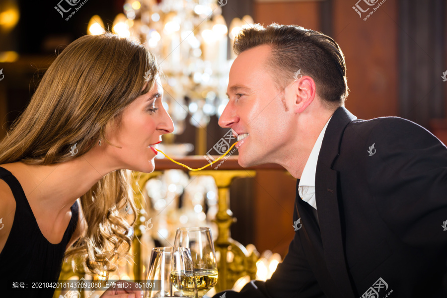 这对幸福的情侣在一家高级餐厅浪漫约会，他们吃意大利面，背景是一盏大吊灯