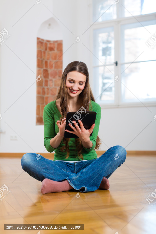 网上约会——年轻女子坐在家里的地板上，用平板电脑通过互联网购买新家具