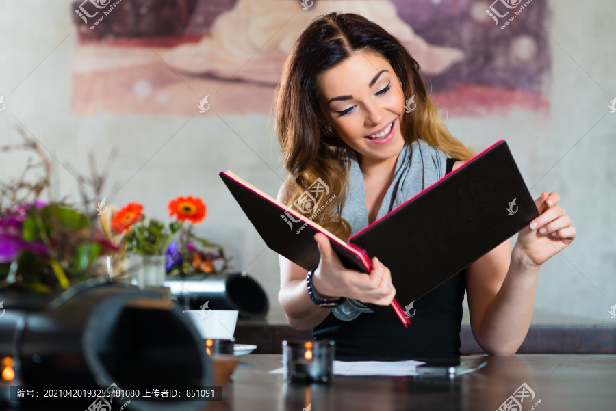 年轻女子在咖啡馆或餐馆里，看着菜单卡，选择