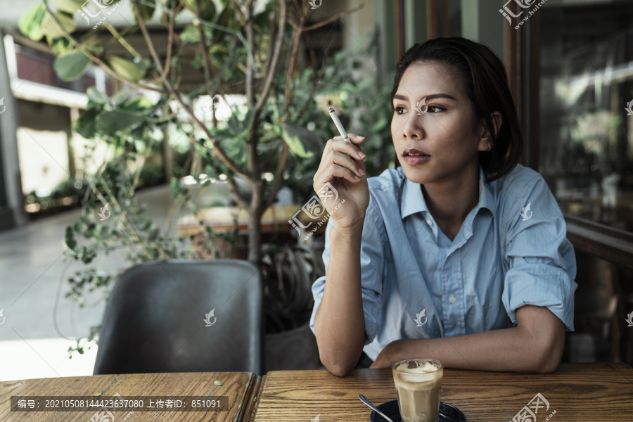 一名亚泰妇女在咖啡馆外手拿香烟抽烟。