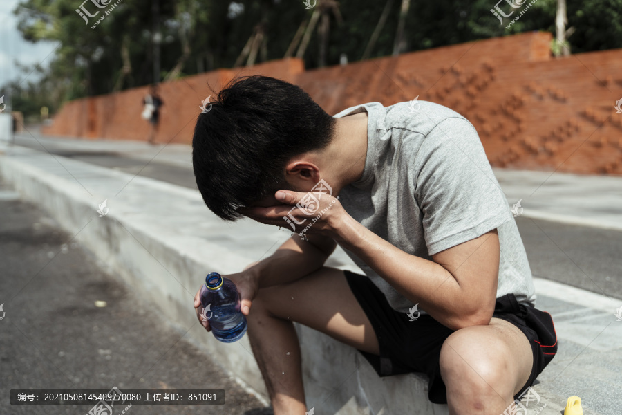 运动男用瓶子里的水洗脸。亚洲年轻人用瓶子里的水洗脸。