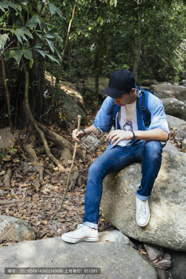 男性徒步旅行者在森林里有大石头的瀑布边休息。