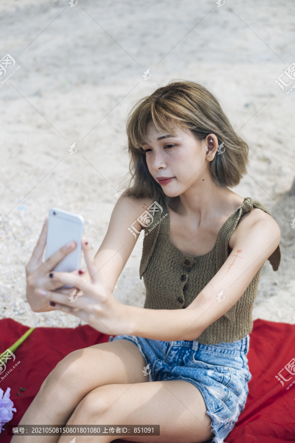短发女孩坐在沙滩上的红垫子上自拍。