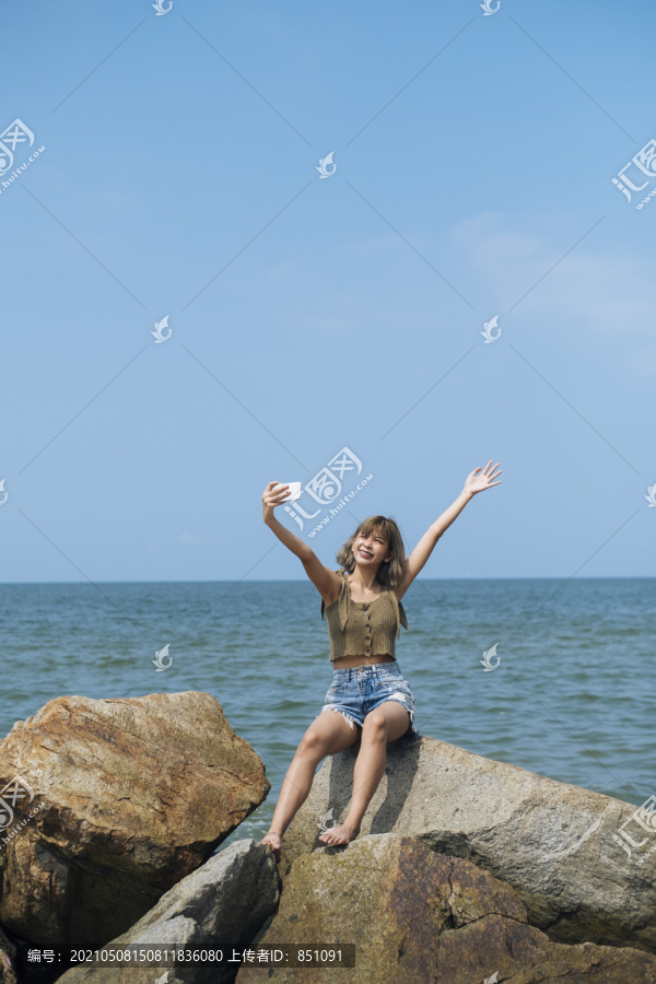 短发女孩站在沙滩上，坐在海边的岩石上自拍。