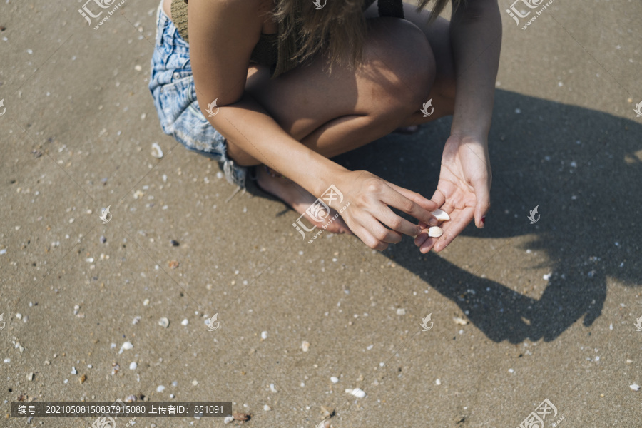 穿着短牛仔裤的短发女孩坐在海边的海滩上收集贝壳。