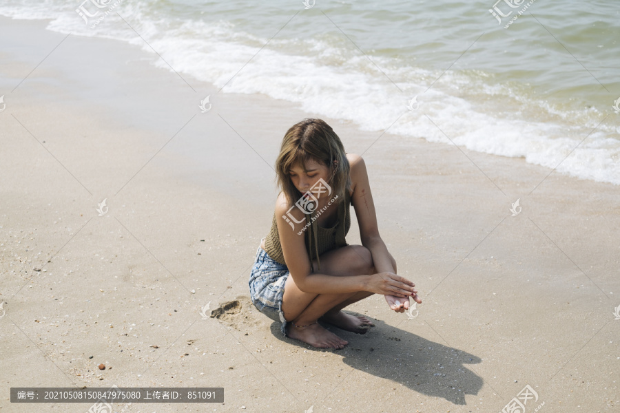 穿着短牛仔裤的短发女孩坐在海边的海滩上收集贝壳。