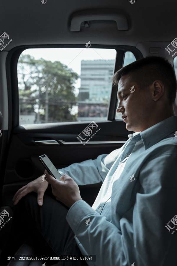 穿着蓝色衬衫的商人在后座查看手机上的信息，心烦意乱。