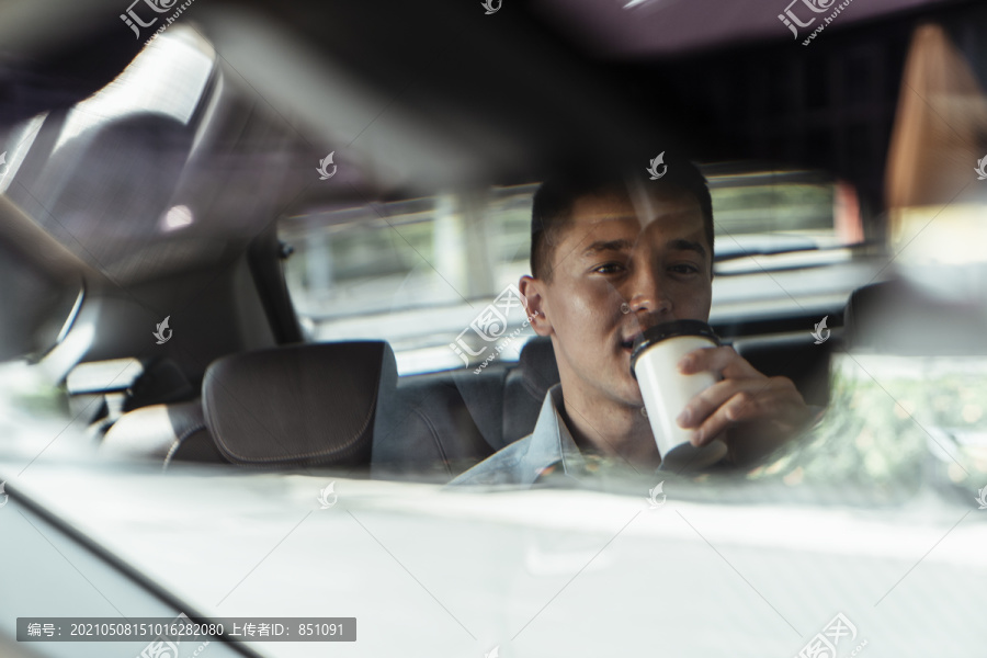 从后视镜中可以看到商人在开车去办公室时喝咖啡的情景。