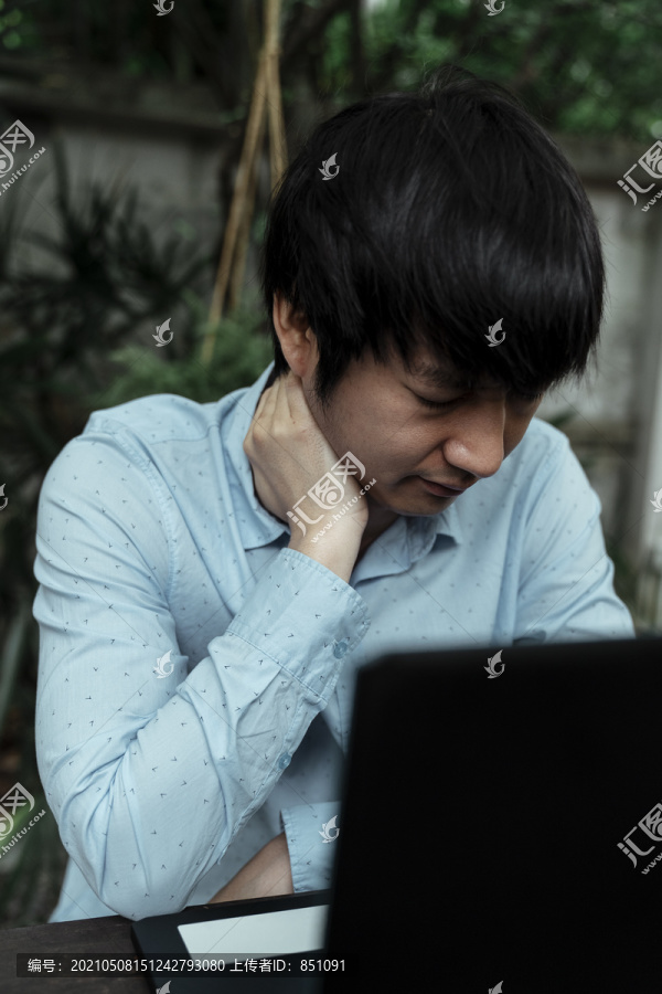 穿蓝衬衫的黑发男人脖子疼是因为工作努力。