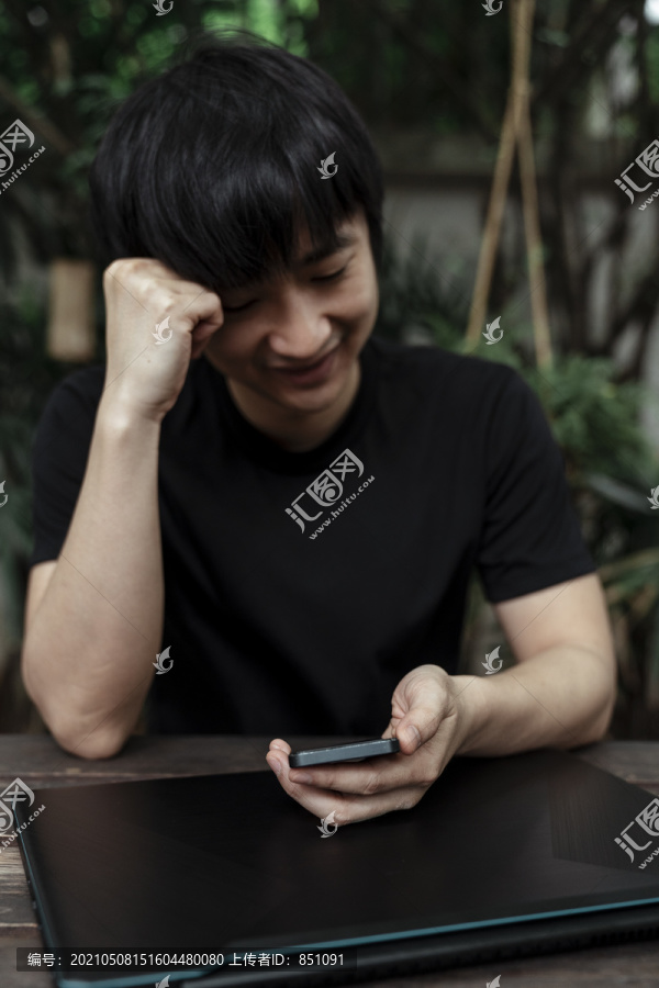 一个穿黑色t恤衫的男人从他的智能手机上读到一些信息后，露出了笑容。