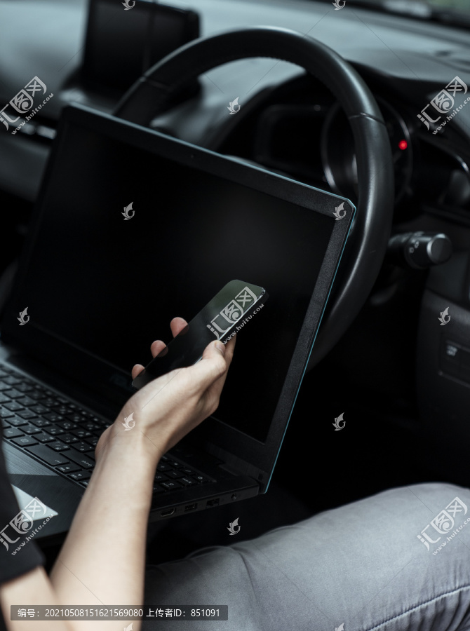 一个男人在车里工作时，智能手机和笔记本电脑的剪影。