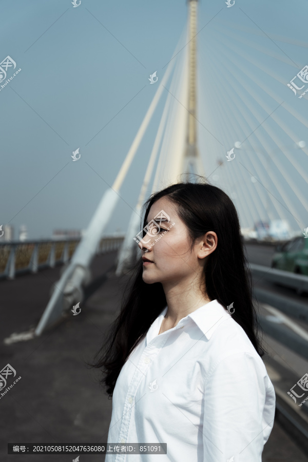 中等镜头的黑色长发女子穿着白衬衫站在桥上在大风天。