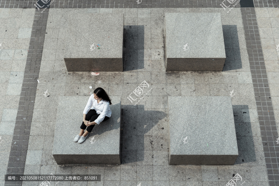 一个女人坐在一块方形岩石上，自己抱着膝盖。