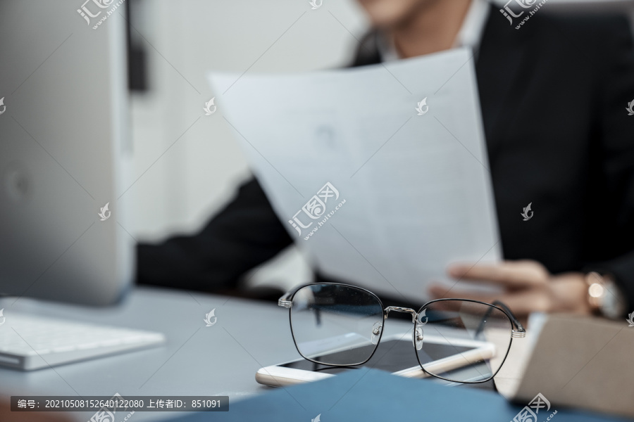 在电脑前拿着纸的商人工作台上的眼镜。男人下班后放松。
