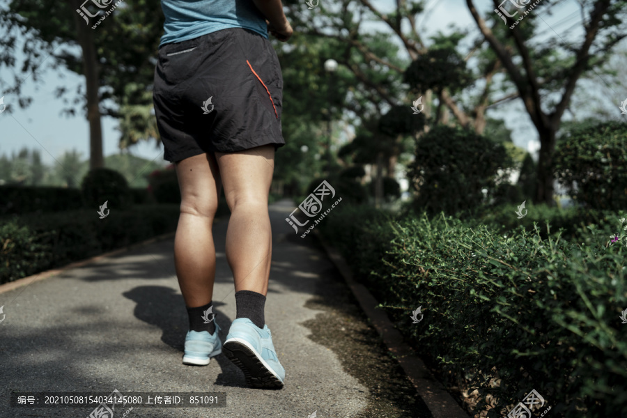 后视图-胖乎乎的运动型亚洲女子穿着蓝色运动服在公园跑道上慢跑。