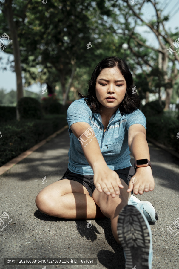 超重的年轻女子在公园里伸腿的画像。