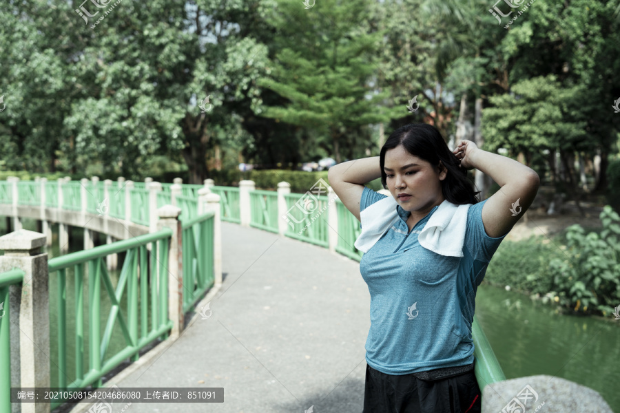 胖乎乎的运动型亚洲女子穿着蓝色运动服在公园跑步后放松。