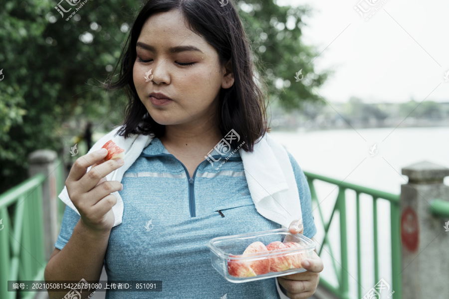 胖乎乎的运动型亚洲女人，穿着蓝色运动服，运动后吃苹果片。