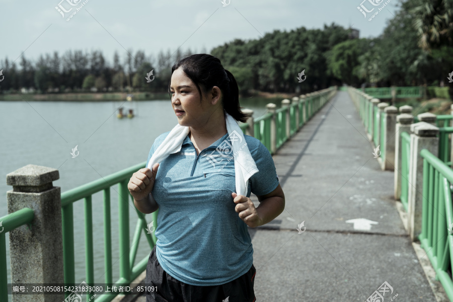 胖乎乎的运动型亚洲女性，穿着蓝色运动服，在大自然的跑道上奔跑。