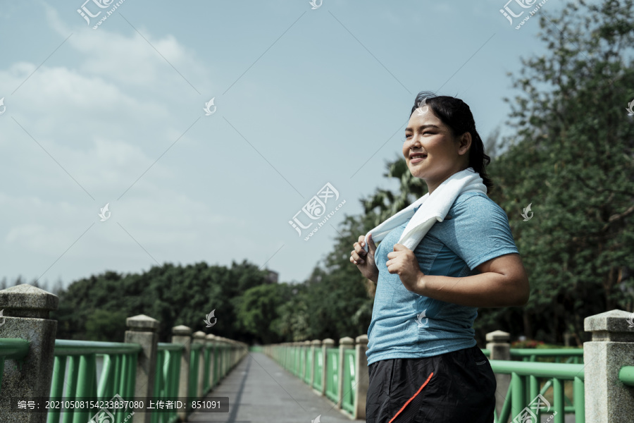 快乐胖胖的运动型亚洲女人，穿着蓝色运动服，在大自然的跑道上奔跑。健康的生活。