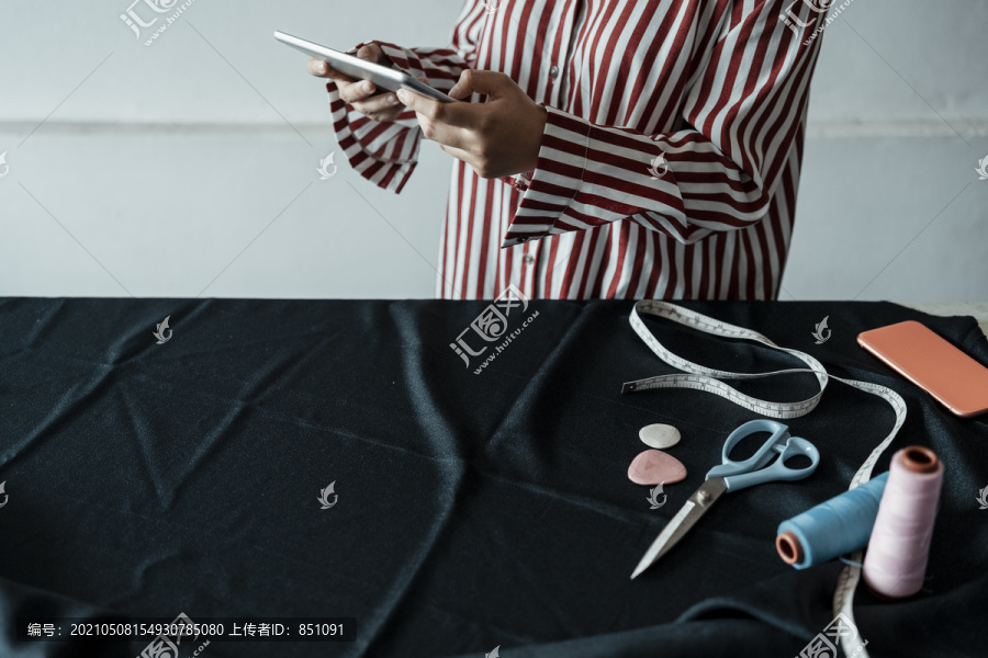 一位年轻的亚洲设计师手持平板电脑在展厅里做衣服。