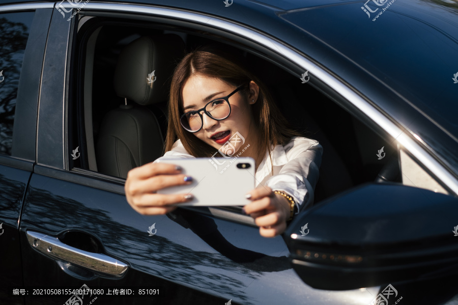 交通和车辆概念-戴眼镜的泰国妇女用智能手机自拍。把手放在车窗外面。
