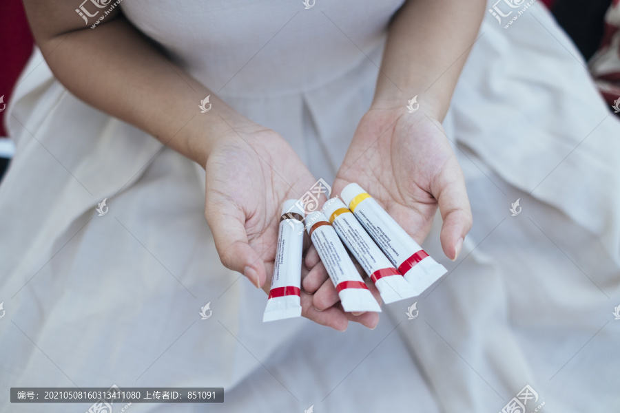 美丽的亚泰艺术家，穿着白色连衣裙，手上拿着彩色的液体水彩管。