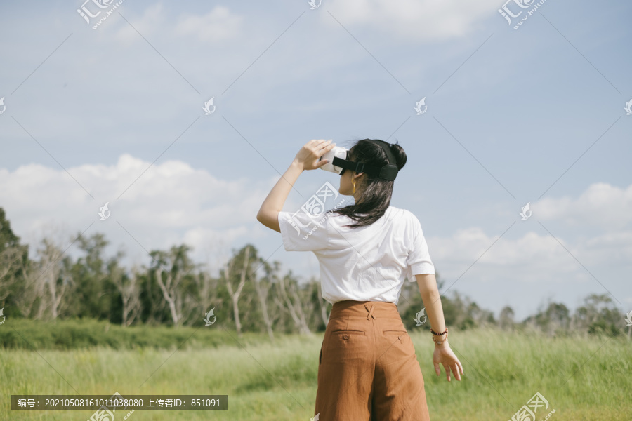 黑色马尾头发的女人穿着休闲服，戴着VR护目镜，在泥泞的草地上旅行，享受虚拟现实技术。