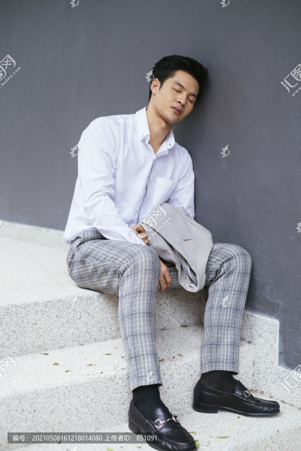 聪明的亚泰商人穿着白领衬衫坐在楼梯上休息，在户外睡觉。