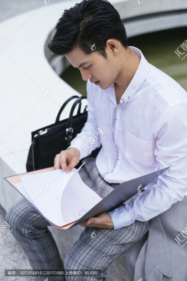 聪明的亚泰商人穿着白领衬衫在户外的文件夹里阅读报告。
