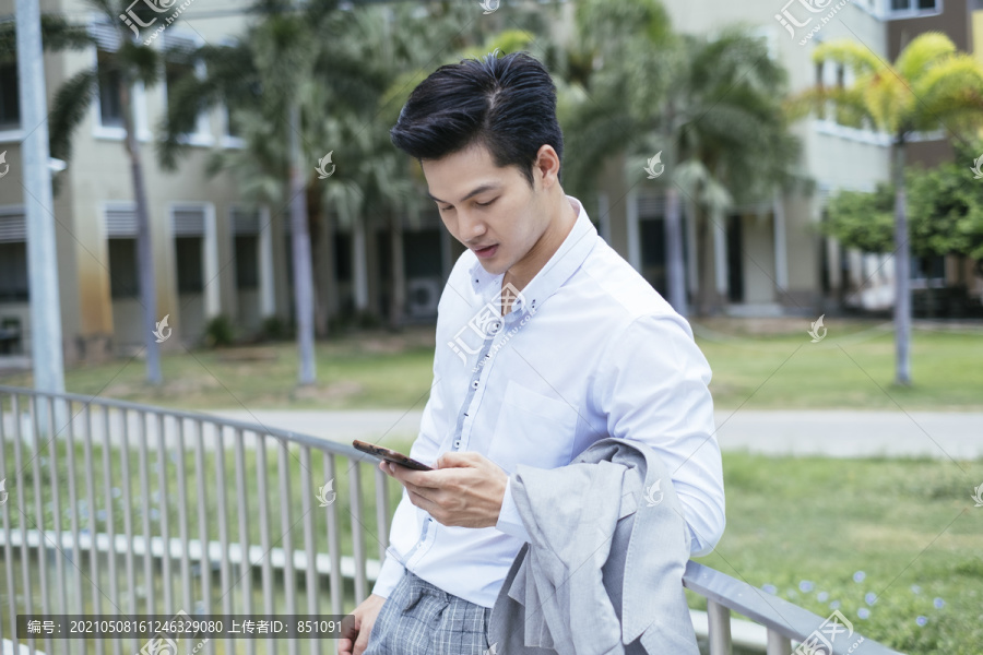 穿着白领衬衫的聪明亚泰商人在公园户外手持智能手机。