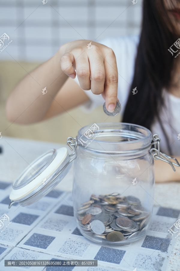 黑色长发女孩把硬币和钞票扔进瓶子里存钱，剪下女人的手和瓶子的形象。