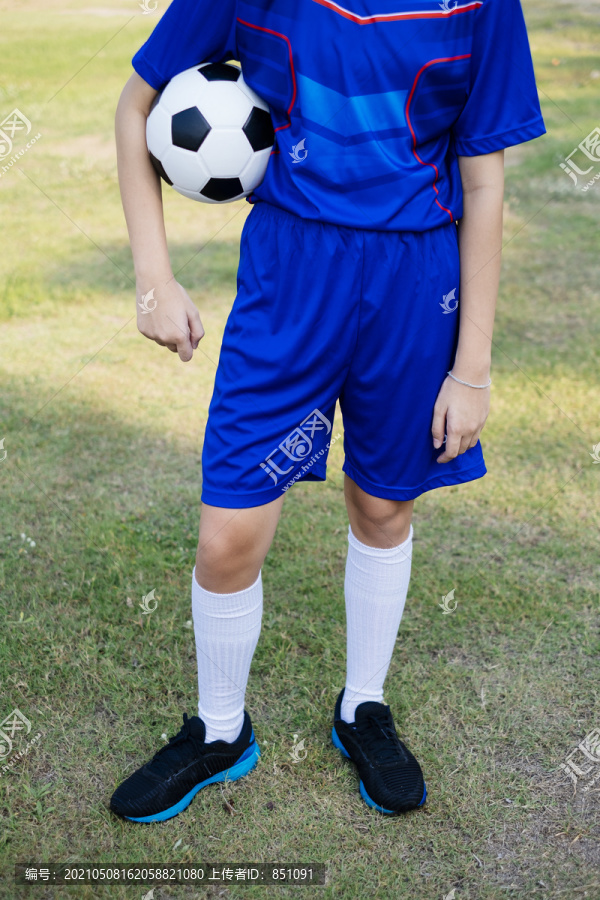 小男孩穿着蓝色足球服，胳膊上抱着球，身体和腿的剪影。