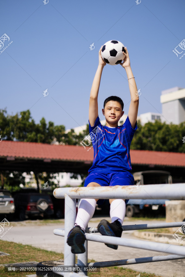 一个男孩坐在扶手上，把足球举到天上。