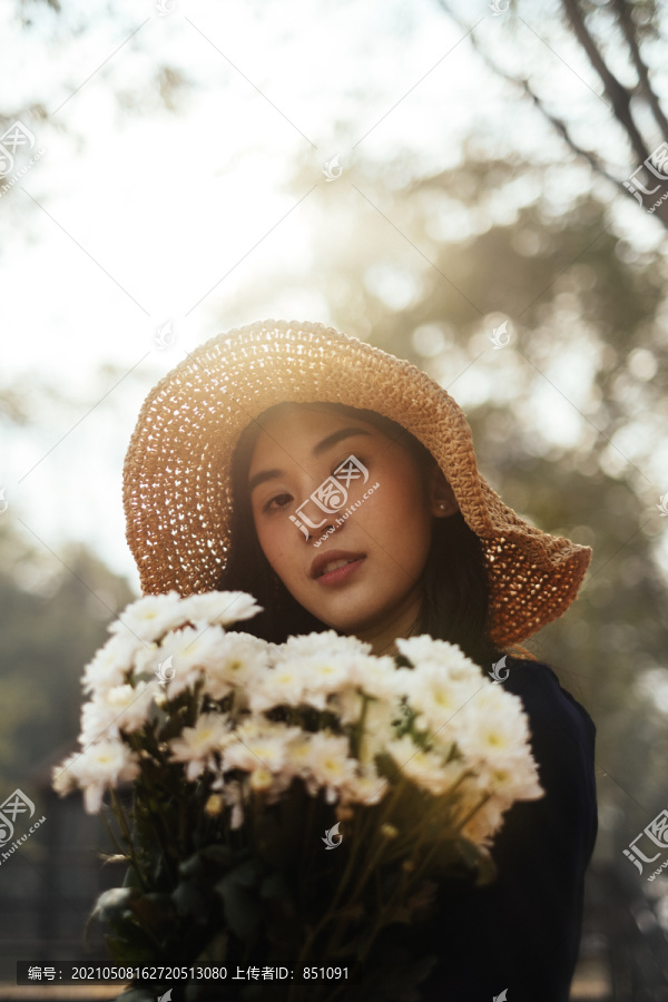 森林中手持白花的美丽女孩的低角度剪影。