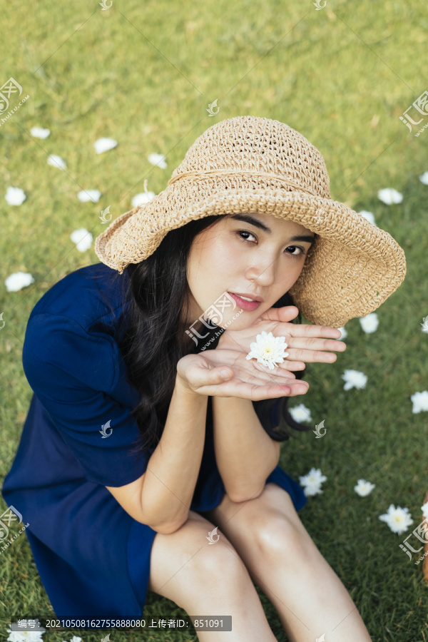 高角度拍摄的可爱女孩穿着深蓝色的裙子坐在田野里的白色花丛中。