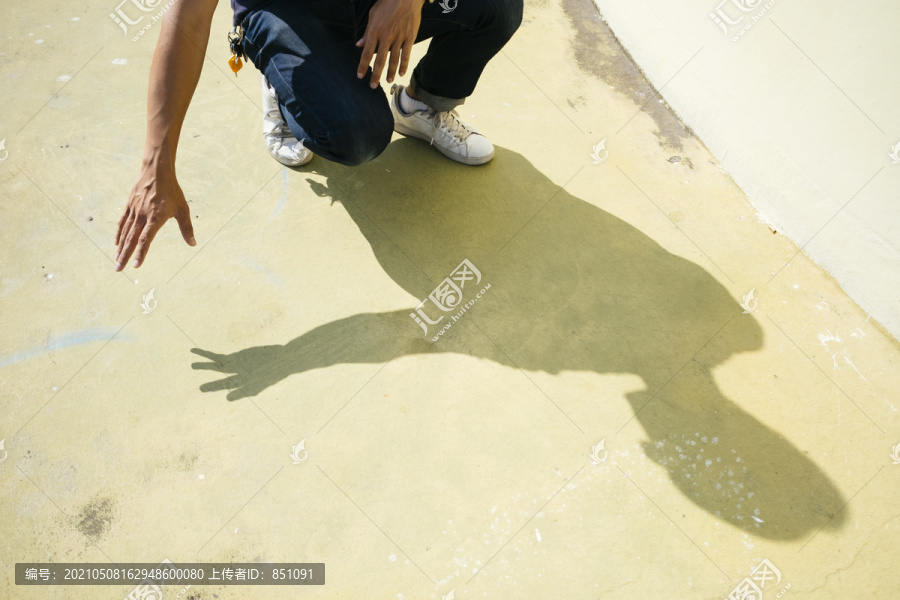 一个男人在阳光下坐在地板上，带着他的影子，这张照片看起来像是要从地板上捡东西。