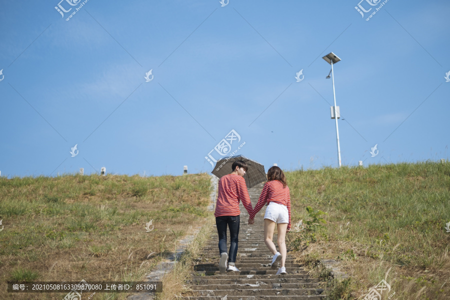 一对十几岁的情侣手拿雨伞，水平地走上石阶。