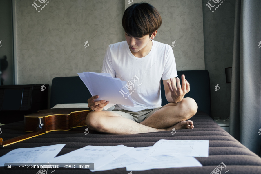 年轻的泰国吉他手在纸上读音乐歌词，边读边用手指练习。